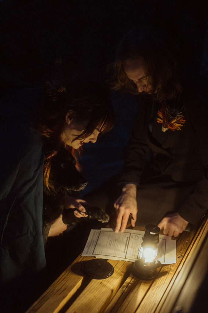 A couple having their dog sign as a witness on their colorado marriage license in the lantern light after their elopement