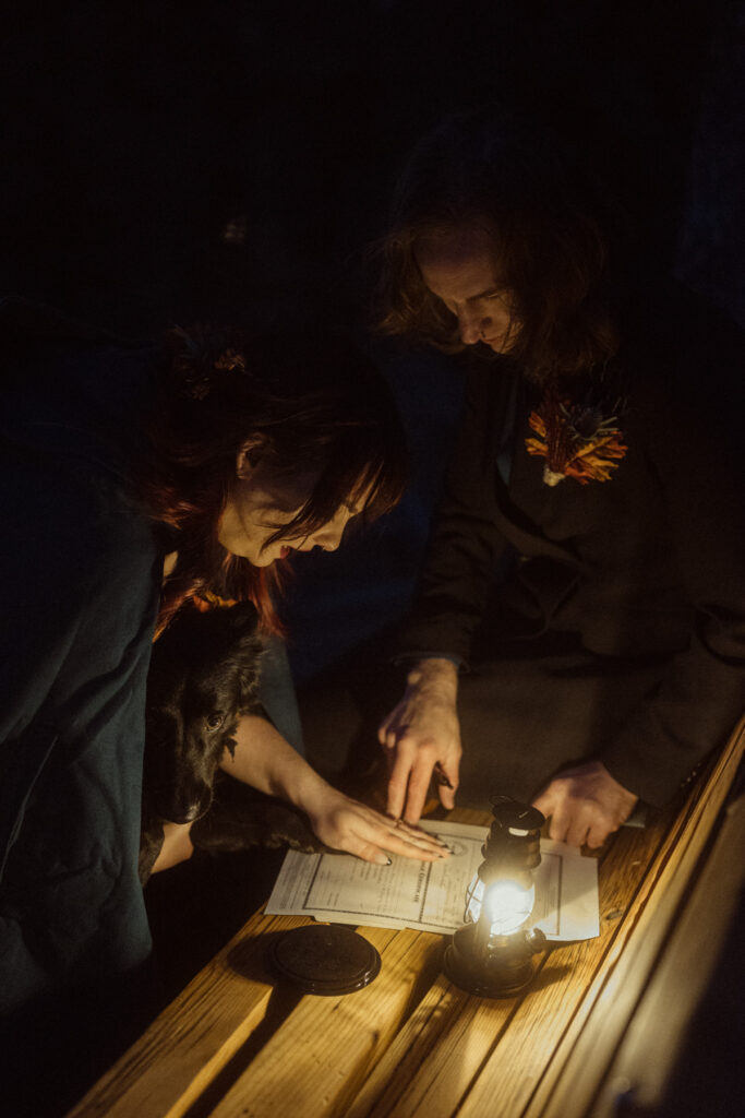 A couple having their dog sign as a witness on their colorado marriage license in the lantern light after their elopement