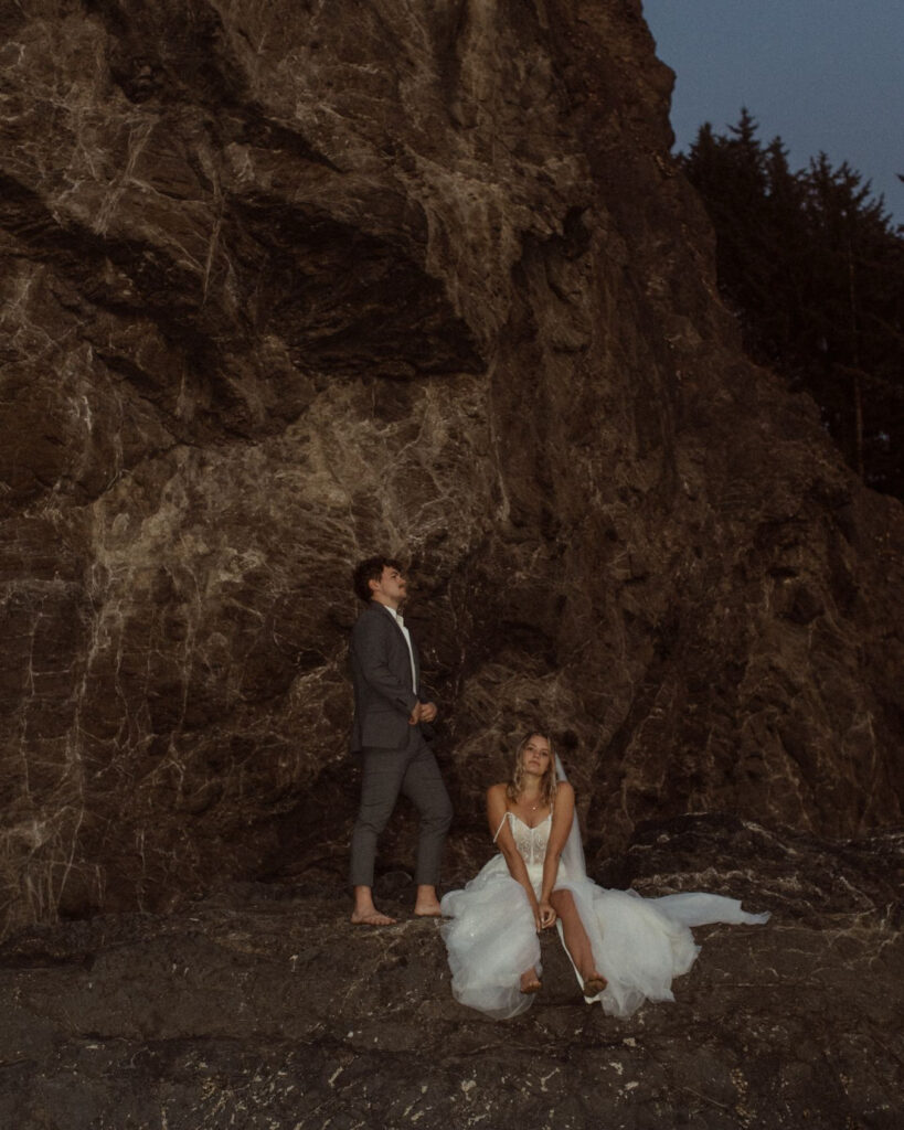 A barefoot wedding couple taking a break on the coastal rocks along Cannon Beach