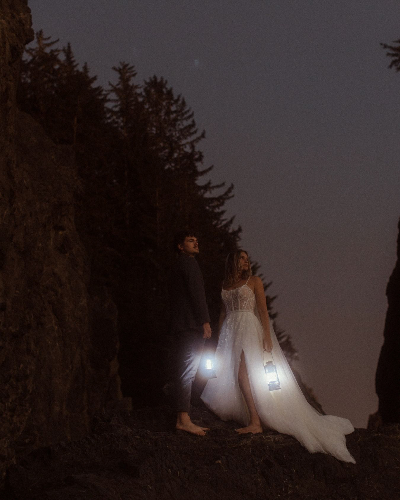 a wedding couple standing on top of a rock along the Oregon Coast with Lanterns