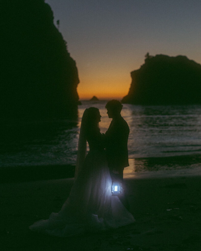 A wedding couple in the sunset holding lanterns after their Cannon Beach Elopement