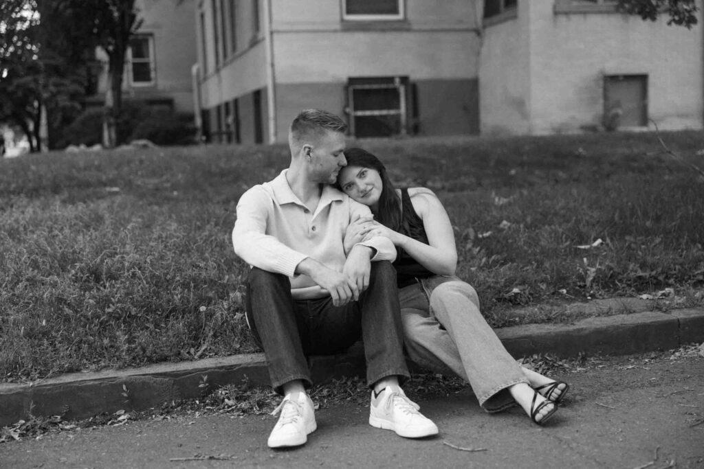 An engaged couple sits together on a curb in downtown Denver on a cool summer day. 