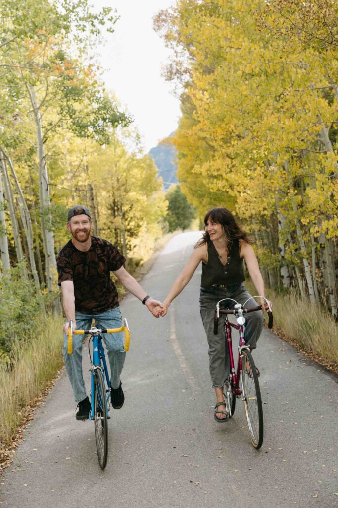 A couple bikes together on vintage road bikes in the fall with Colorado aspens in the background during their engagement session